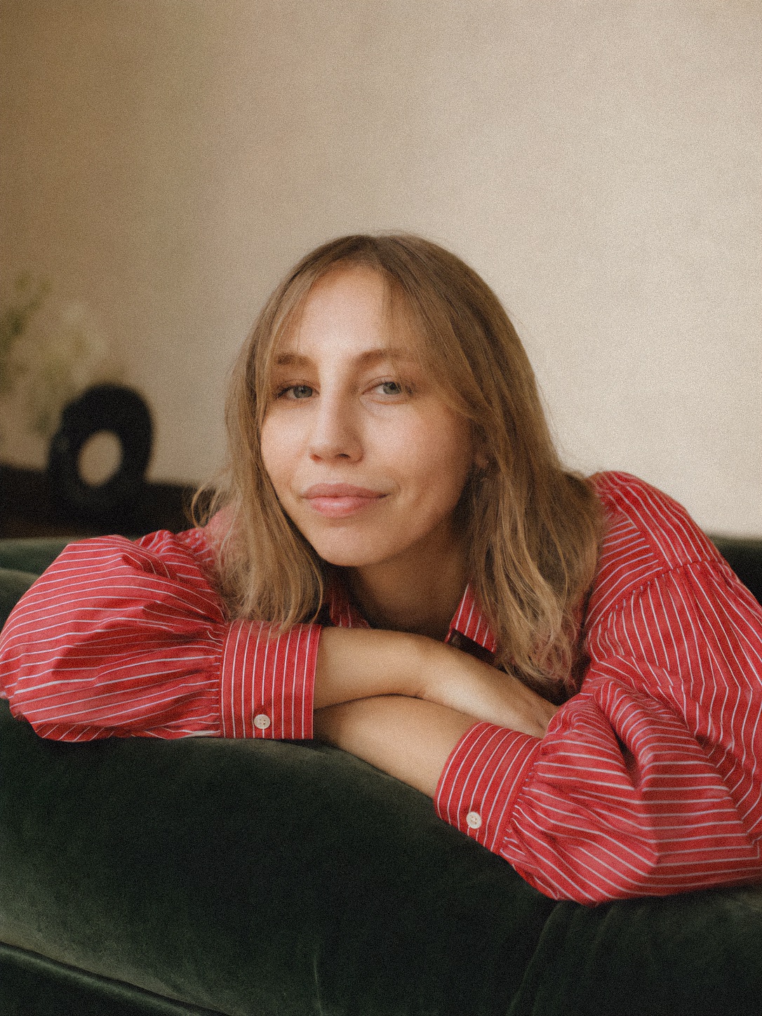 Helin Erdoğrul wearing a red striped shirt and leaning on a dark green sofa